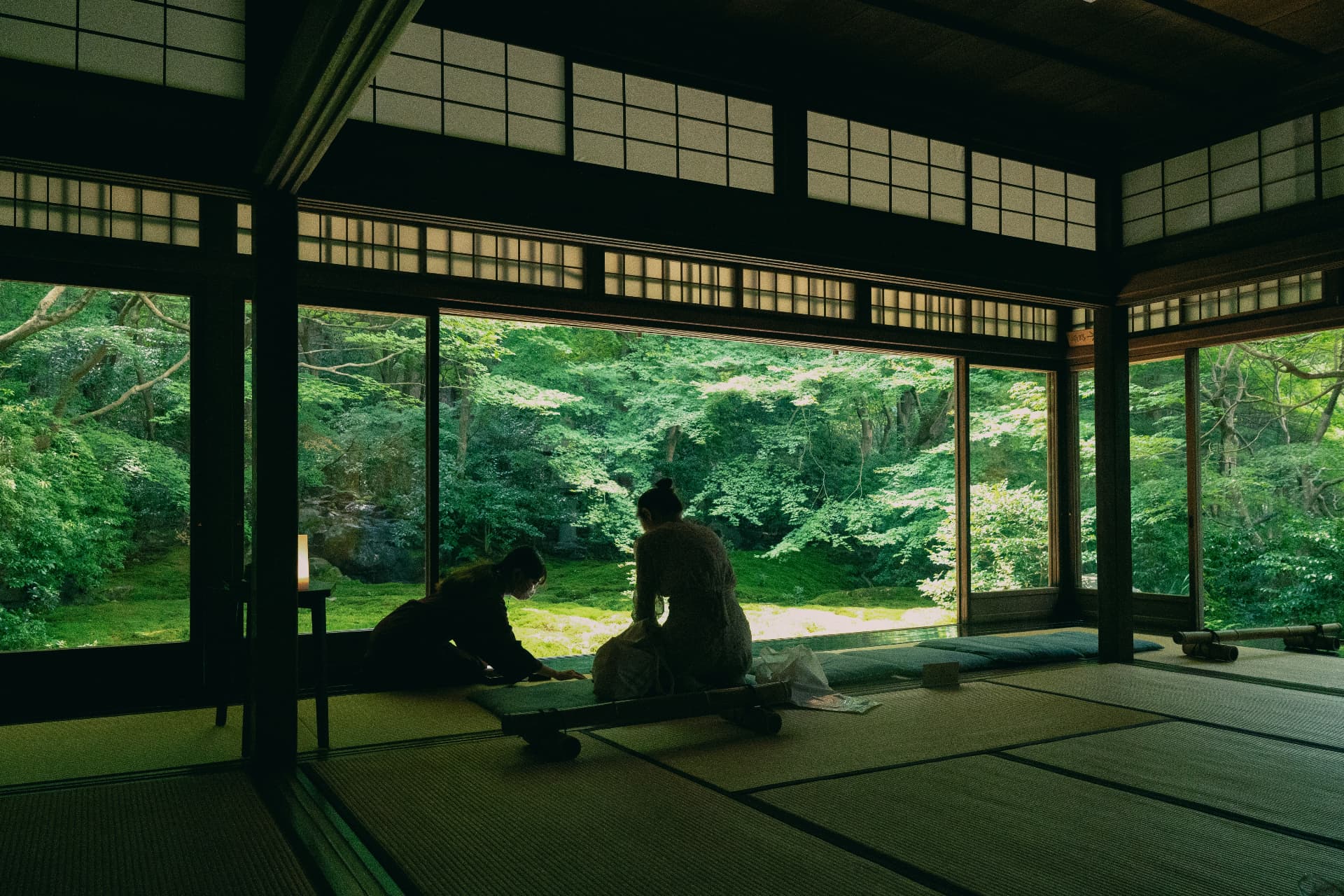 Two people sitting quietly on tatami facing a green garden